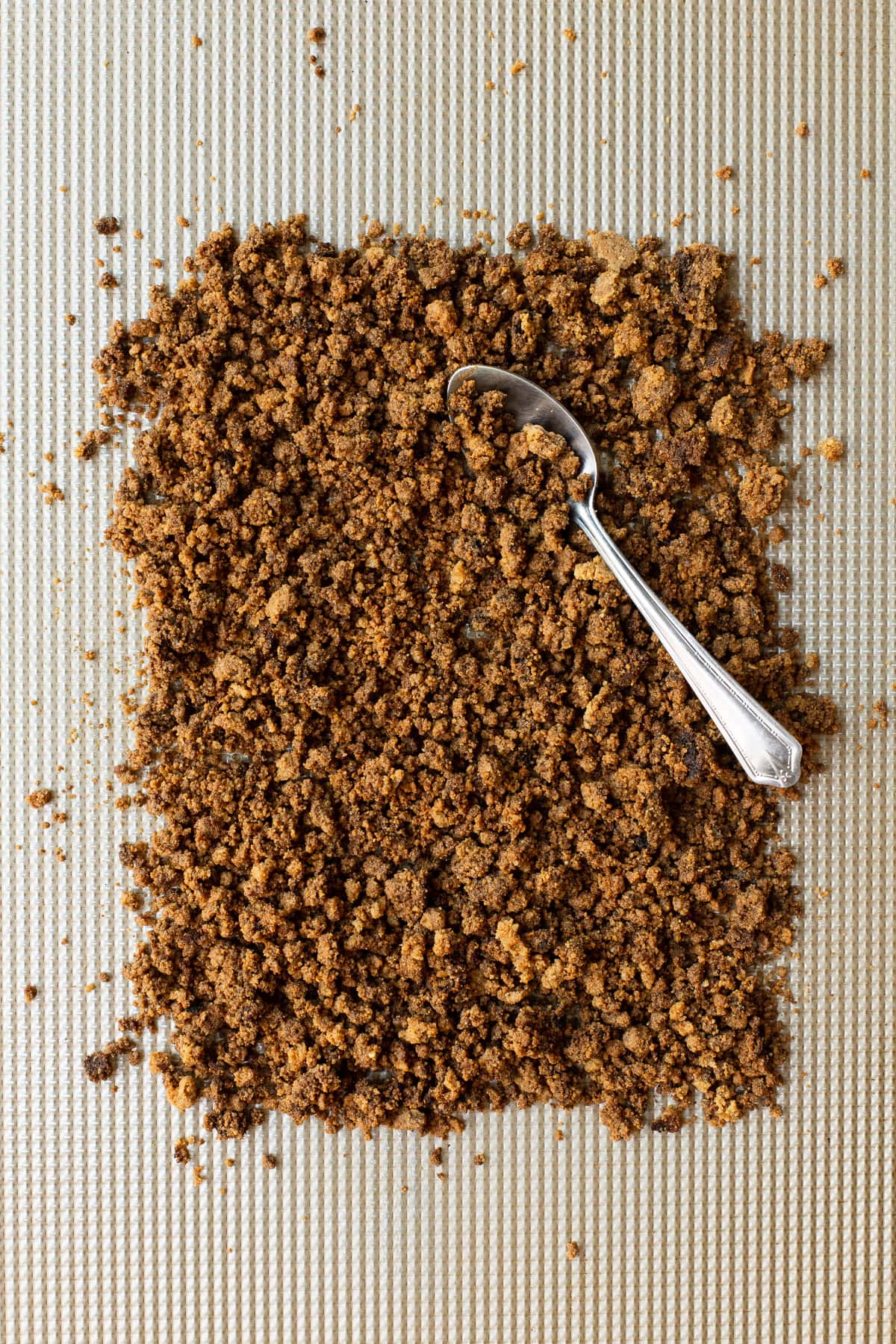 Graham cracker crumbs on a metal pan with a spoon.