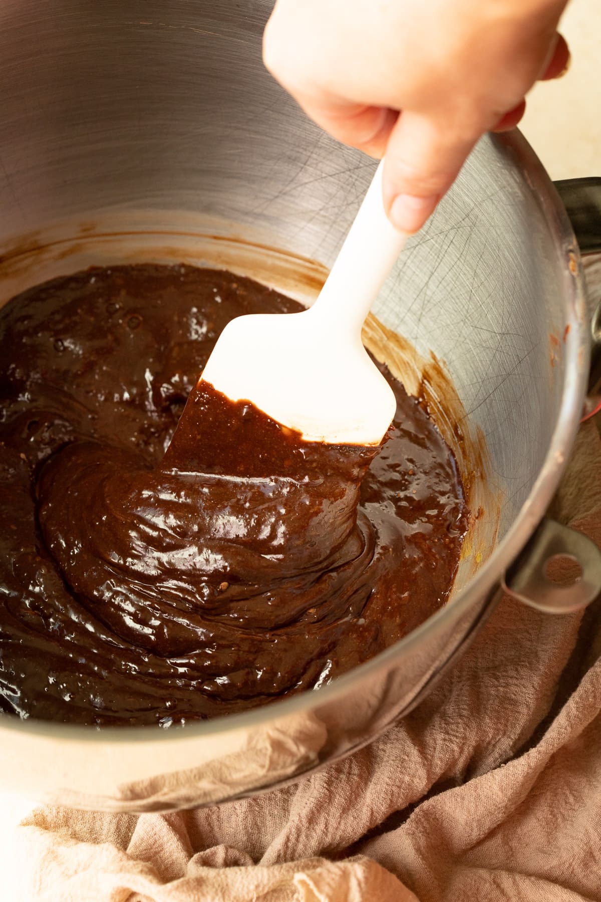 Brownie batter being mixed together in a metal bowl with a rubber spatula.
