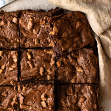 Brownies sliced into squares on a wooden board covered in parchment paper.