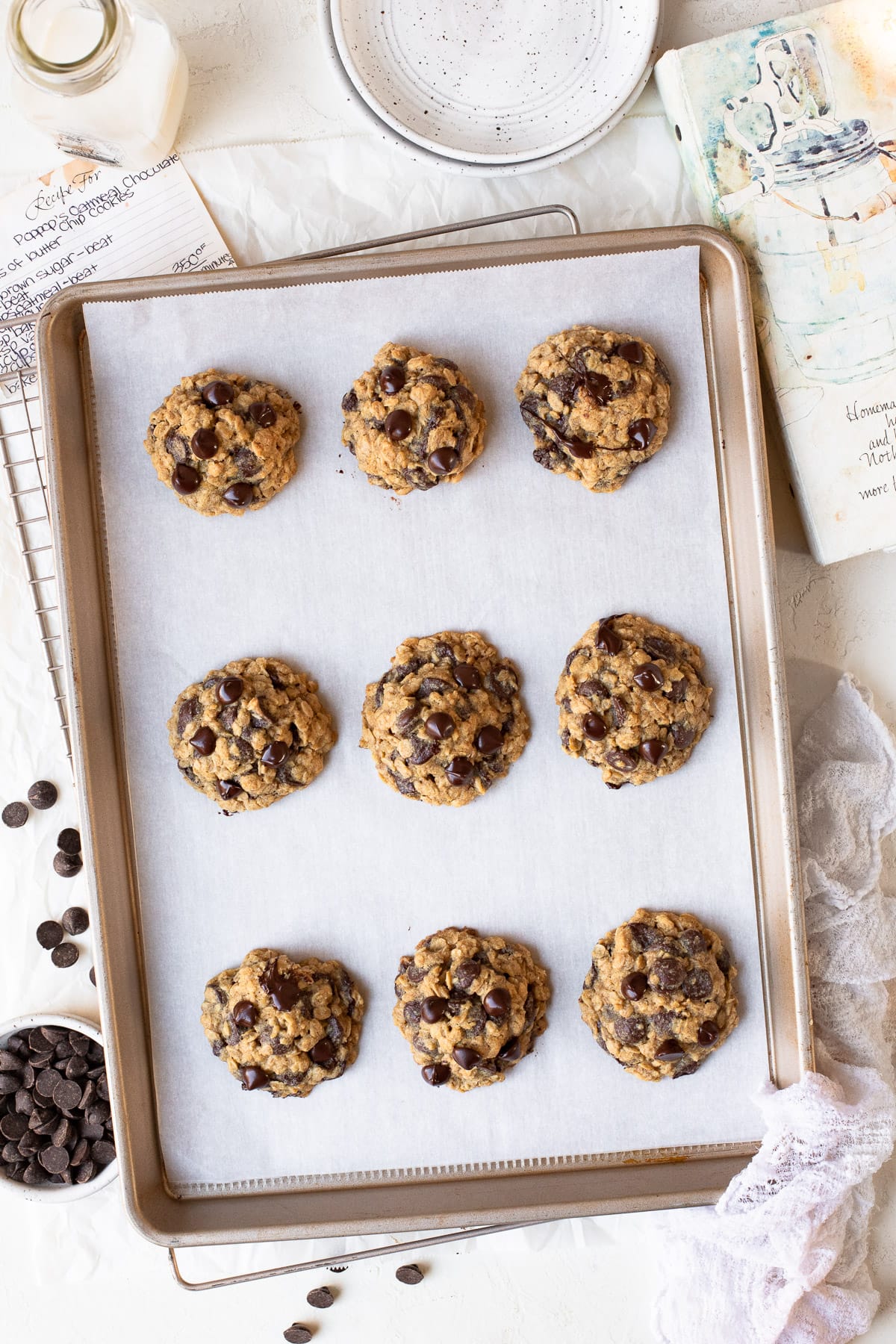 Freshly-baked oatmeal chocolate chip cookies on a parchment-lined baking sheet.