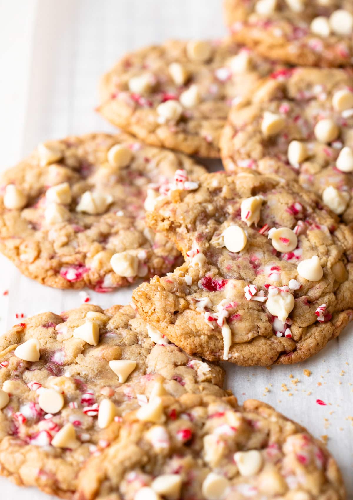 White chocolate peppermint cookies scattered on parchment paper, with a bite taken out of one.
