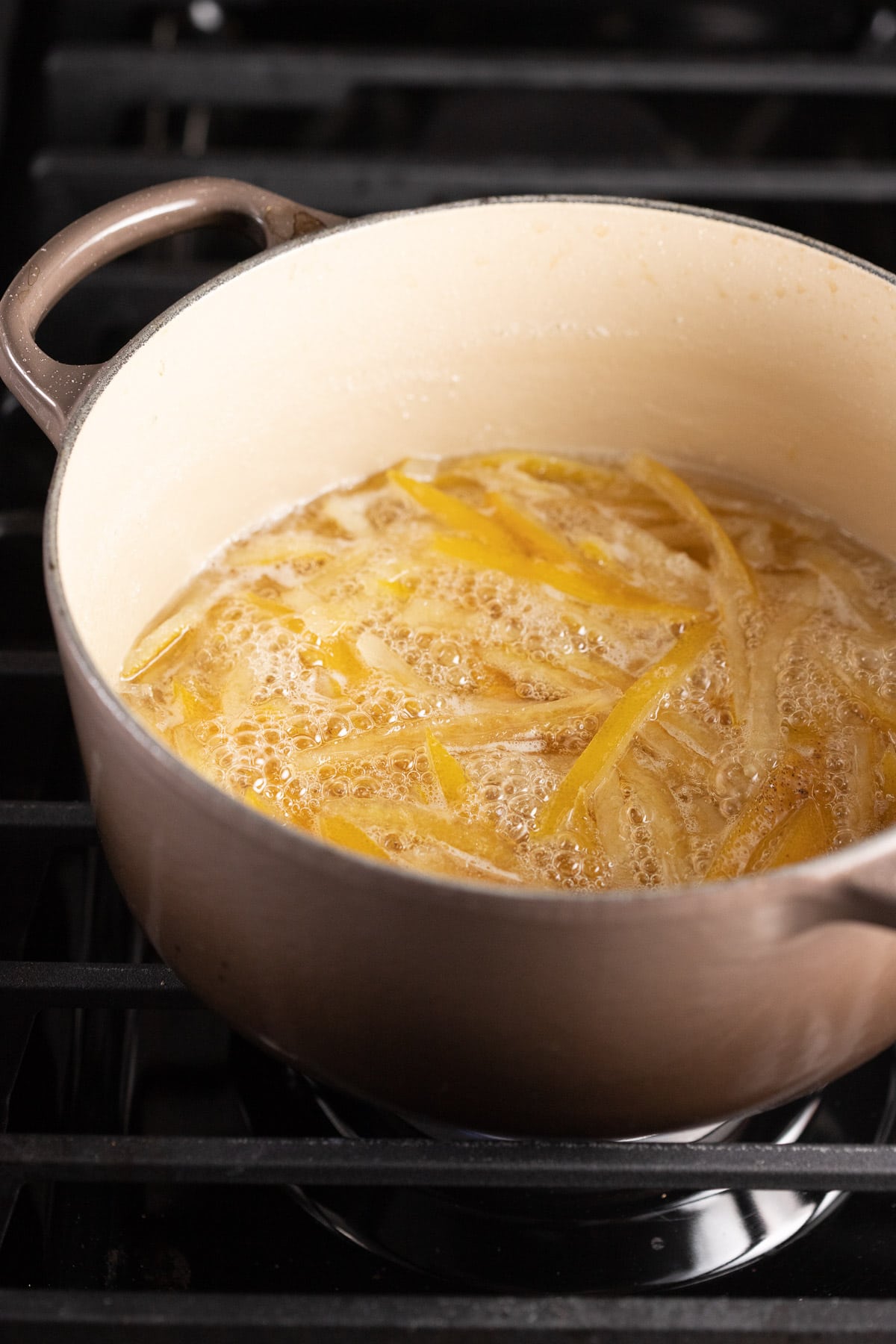 Lemon peel simmering in a sugar syrup on the stove, with the peels getting translucent.