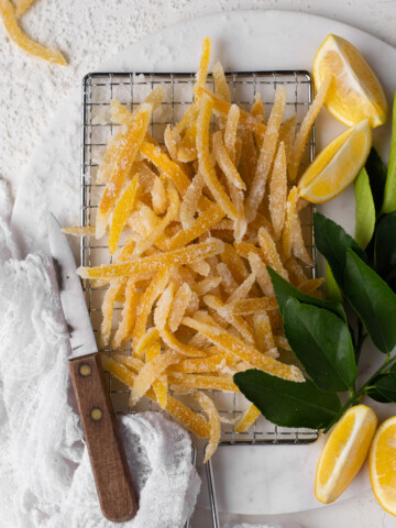 Lemon peel candy on a safety grater with a knife and fresh lemon slices.