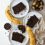 Banana bread slices on plates with ripe bananas and iced coffee.