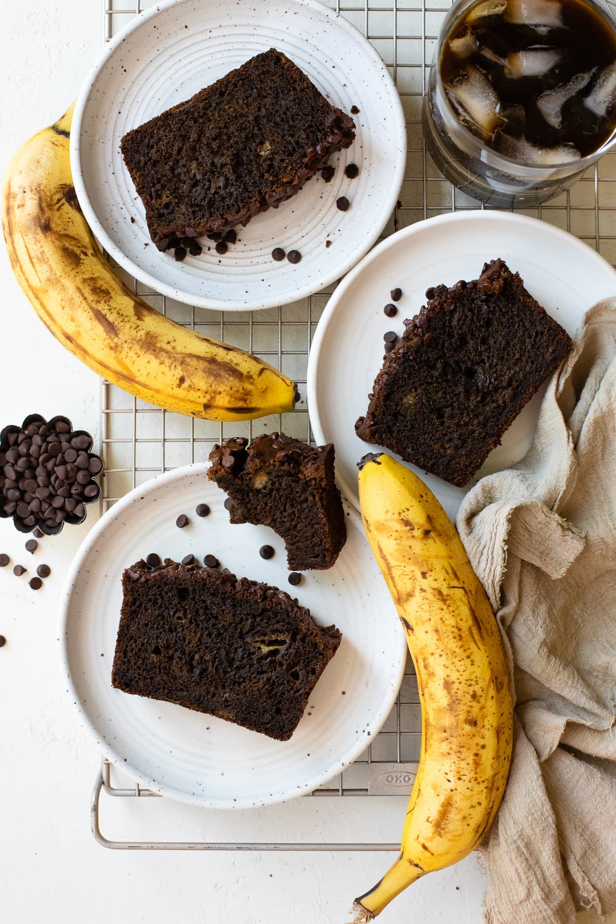 Banana bread slices on plates with ripe bananas and iced coffee.