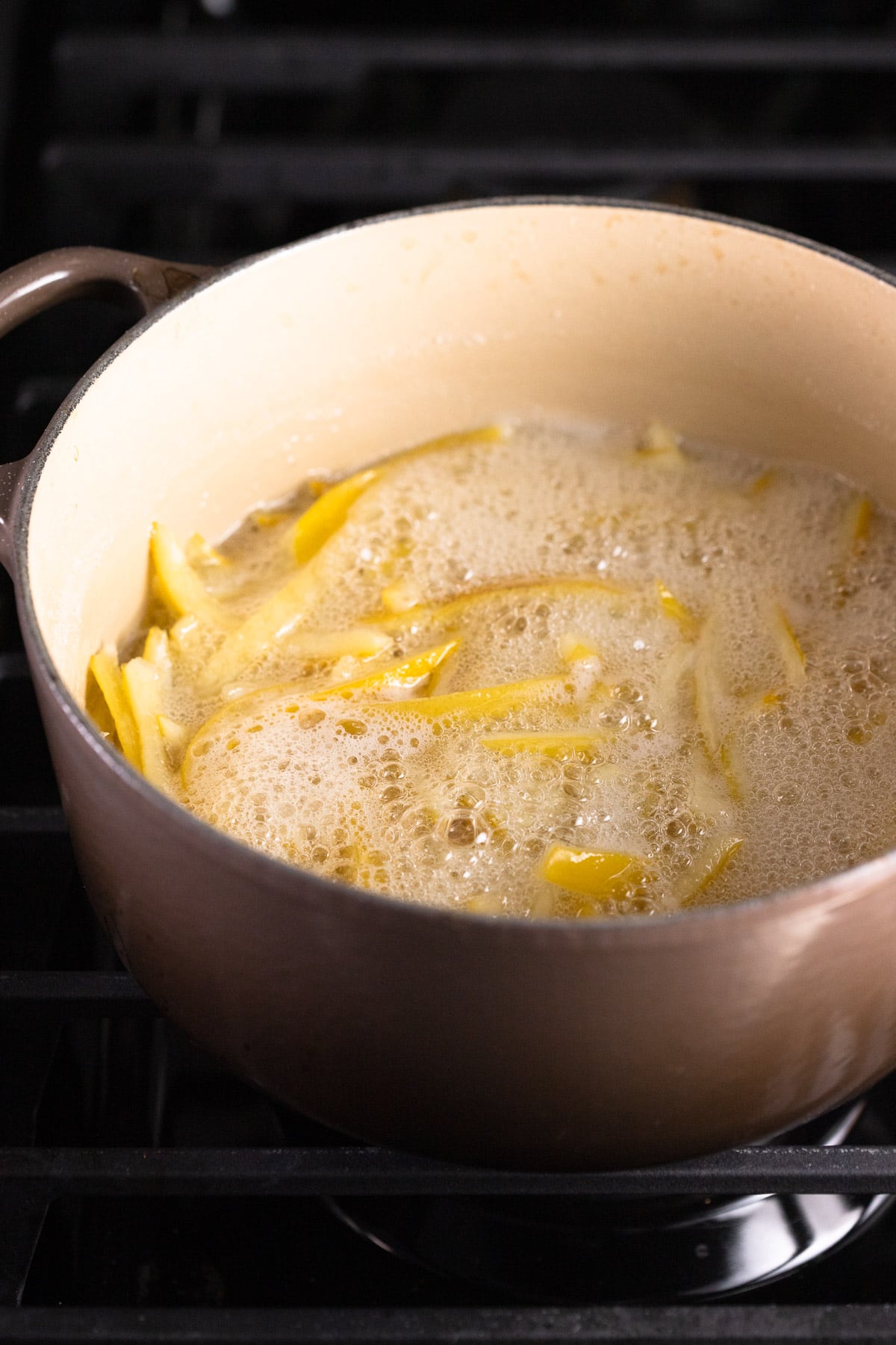 Lemon peels simmering in a sugar syrup on the stove.