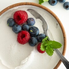 Close up of dairy-free whipped cream in a bowl with fresh berries and mint.