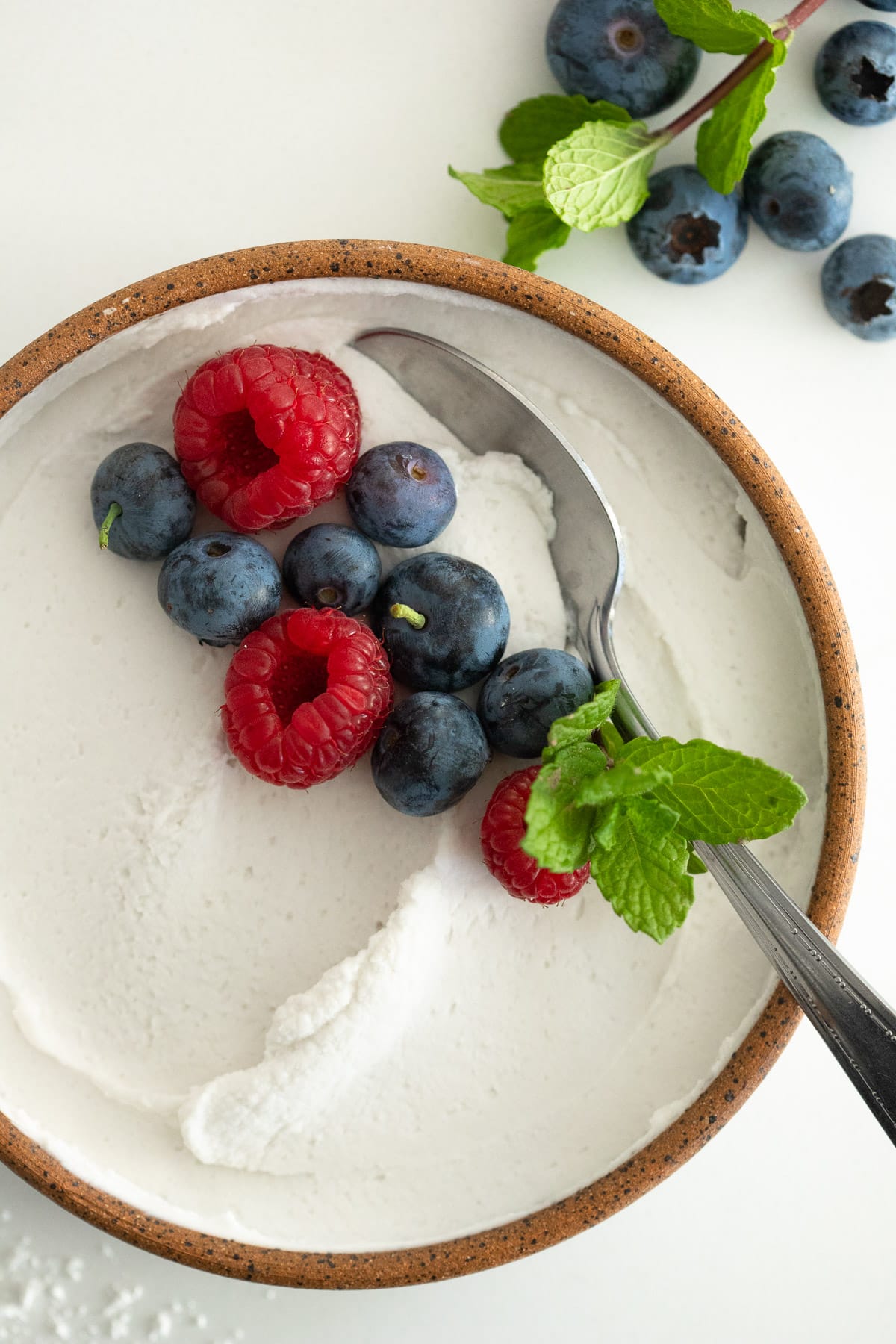 Close up of dairy-free whipped cream in a bowl with fresh berries and mint.
