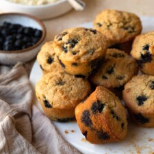 Almond flour blueberry muffins stacked on a round marble cutting board.