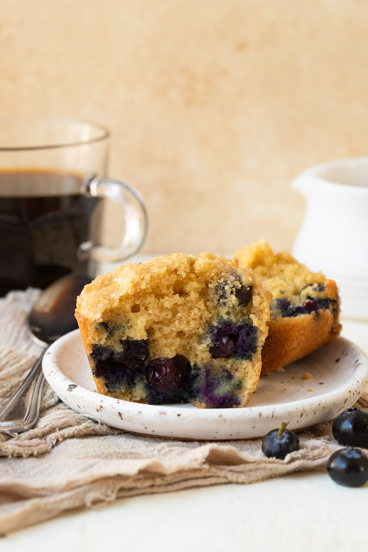 Blueberry almond flour muffin cut in half on a small white plate, served with coffee.