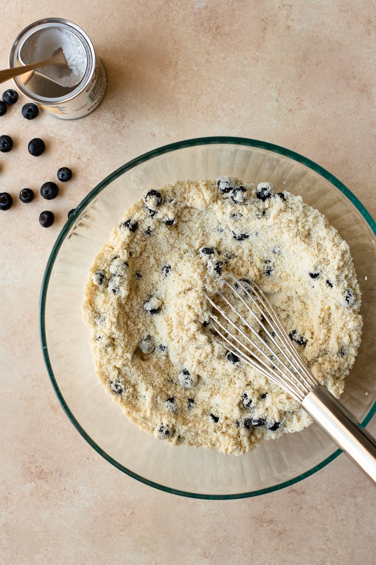 Almond flour, tapioca starch, baking powder, salt, lemon zest, and blueberries whisked together in a glass bowl.