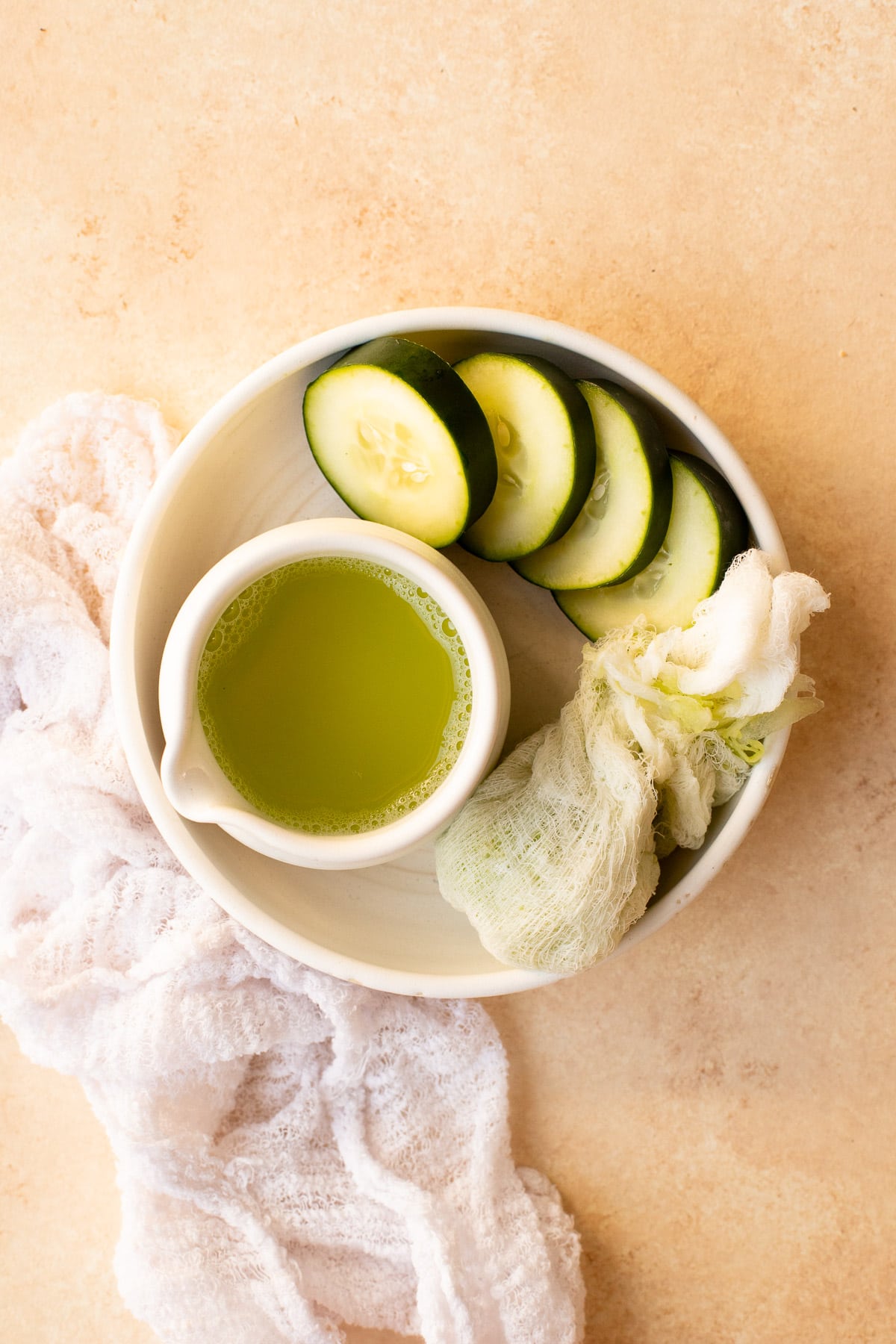 Fresh cucumber juice in a small white container, surrounded by cucumber slices.