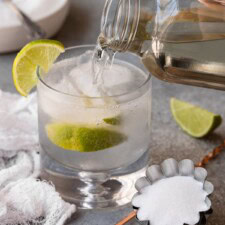 Sugar syrup being poured into a cocktail garnished with lime.