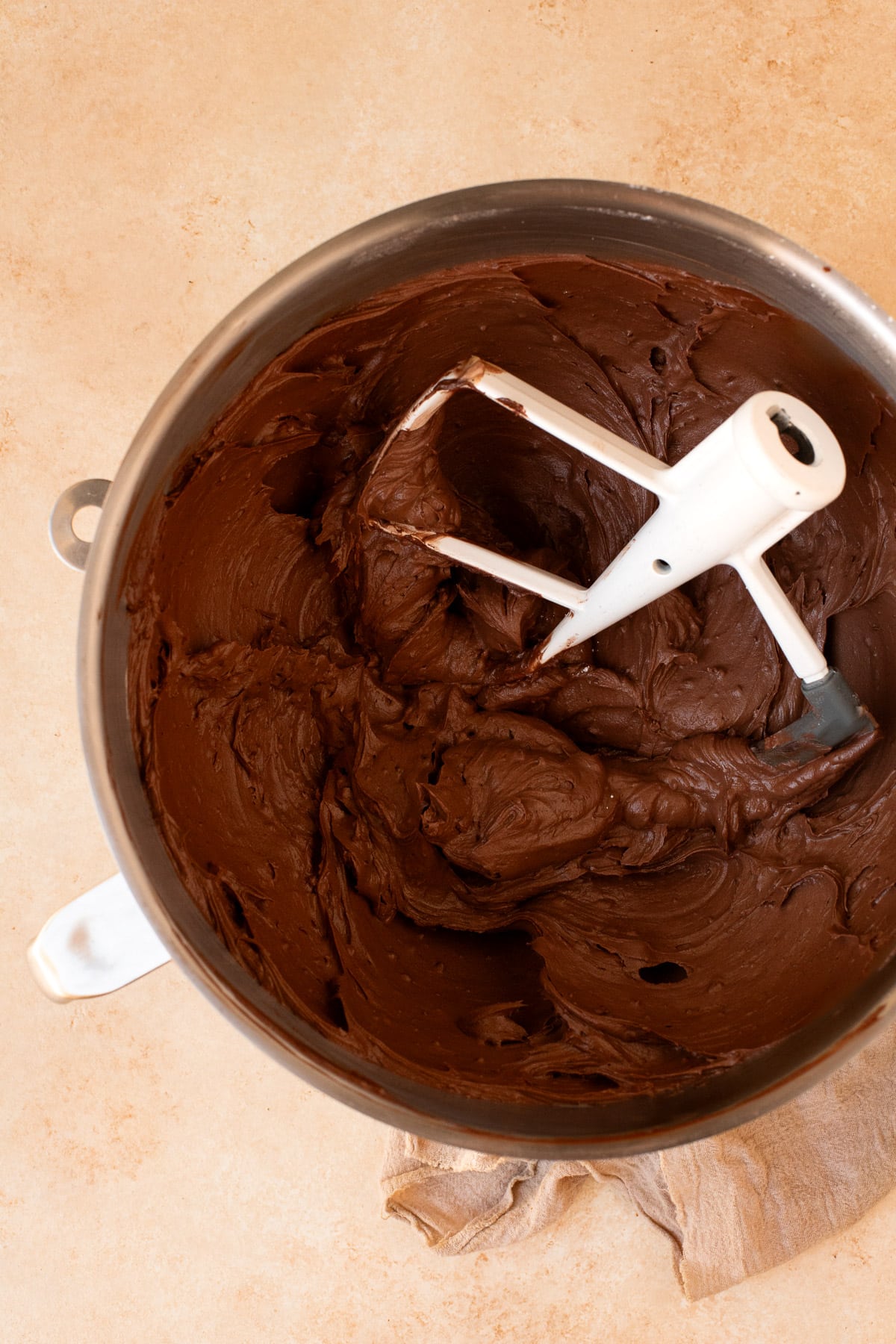 Chocolate frosting in the bowl of a stand mixer with the paddle attachment.