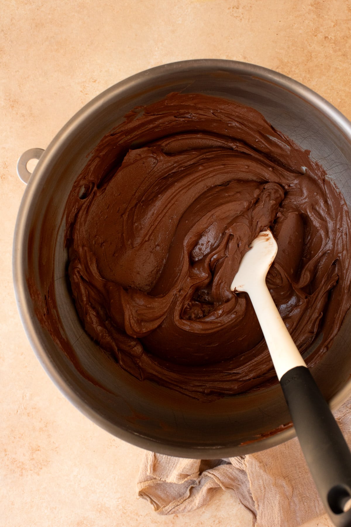 Chocolate frosting mixed together in a large metal bowl with a rubber spatula.