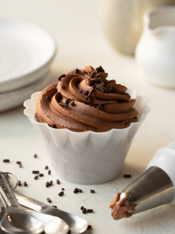 A small bowl filled with piped chocolate whipped cream, with a piping bag to the side.