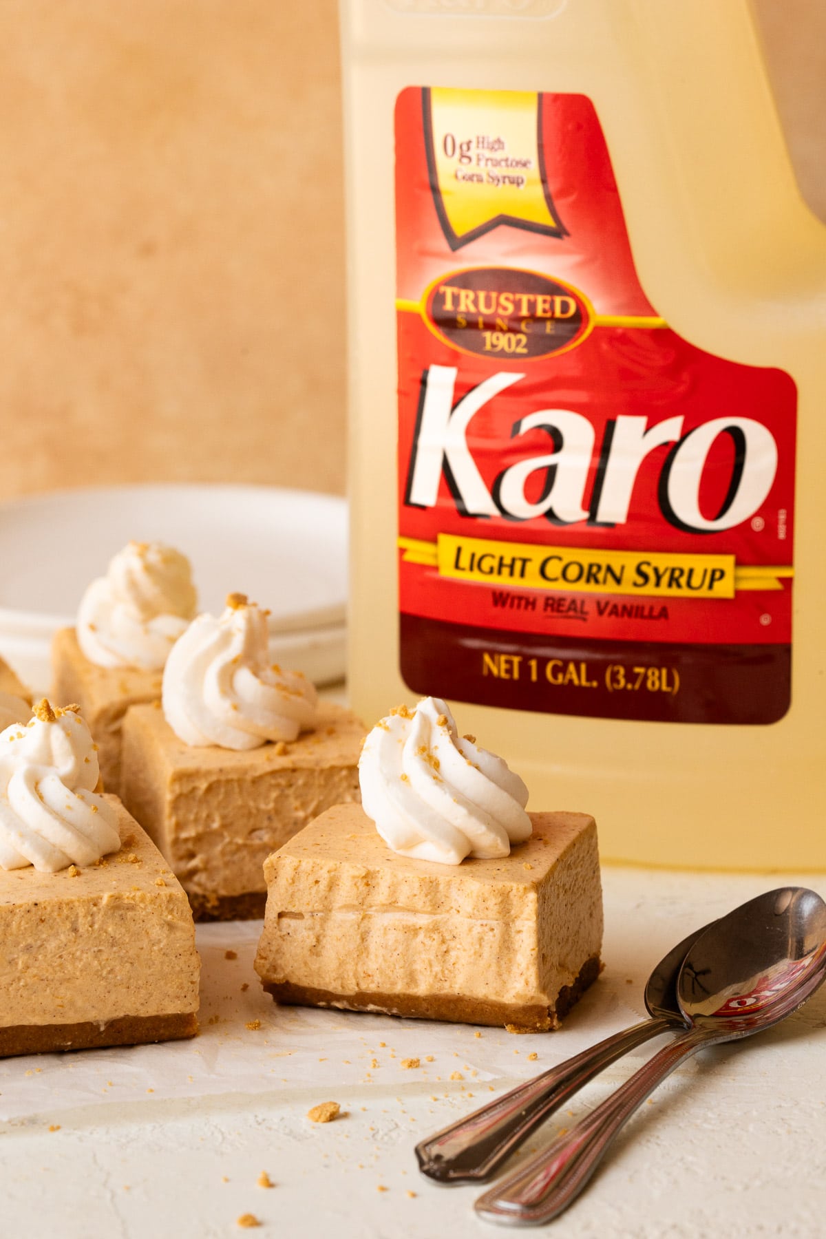 Pumpkin cheesecake bars sliced and topped with whipped cream in front of a bottle of Karo syrup.