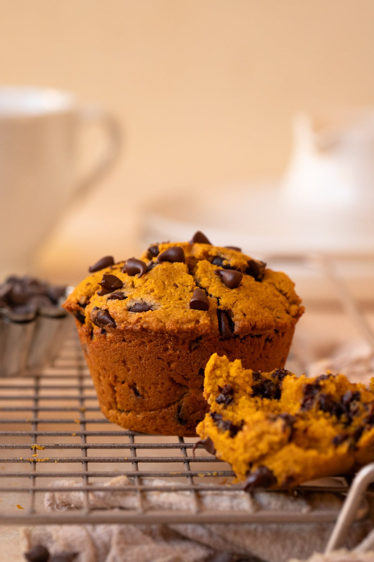 Close up of a muffin on a wire cooling rack, with a portion of a third muffin in the foreground showing the crumb.