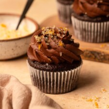 A cupcake with a bowl of orange-infused sparkling sugar in the background.