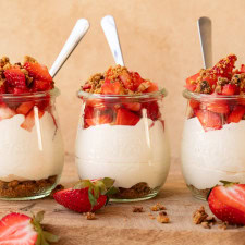 Three strawberry cheesecake cups in small glass jars served with mini spoons.