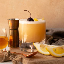 A fully assembled Disaronno sour with a frothy top, garnished with a cocktail cherry and lemon twist.