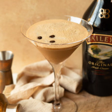 Espresso martini garnished with coffee beans and a bottle of Baileys in the background.
