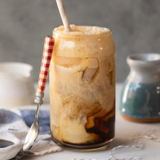 Cream swirling into an iced coffee soda in a glass tumbler.