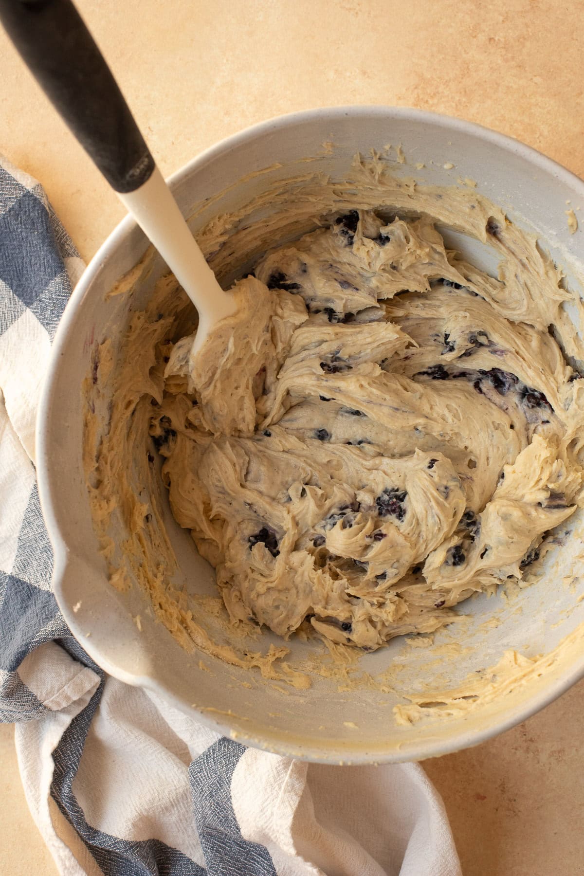 Blackberries being folded into muffin batter in a bowl with a rubber spatula.