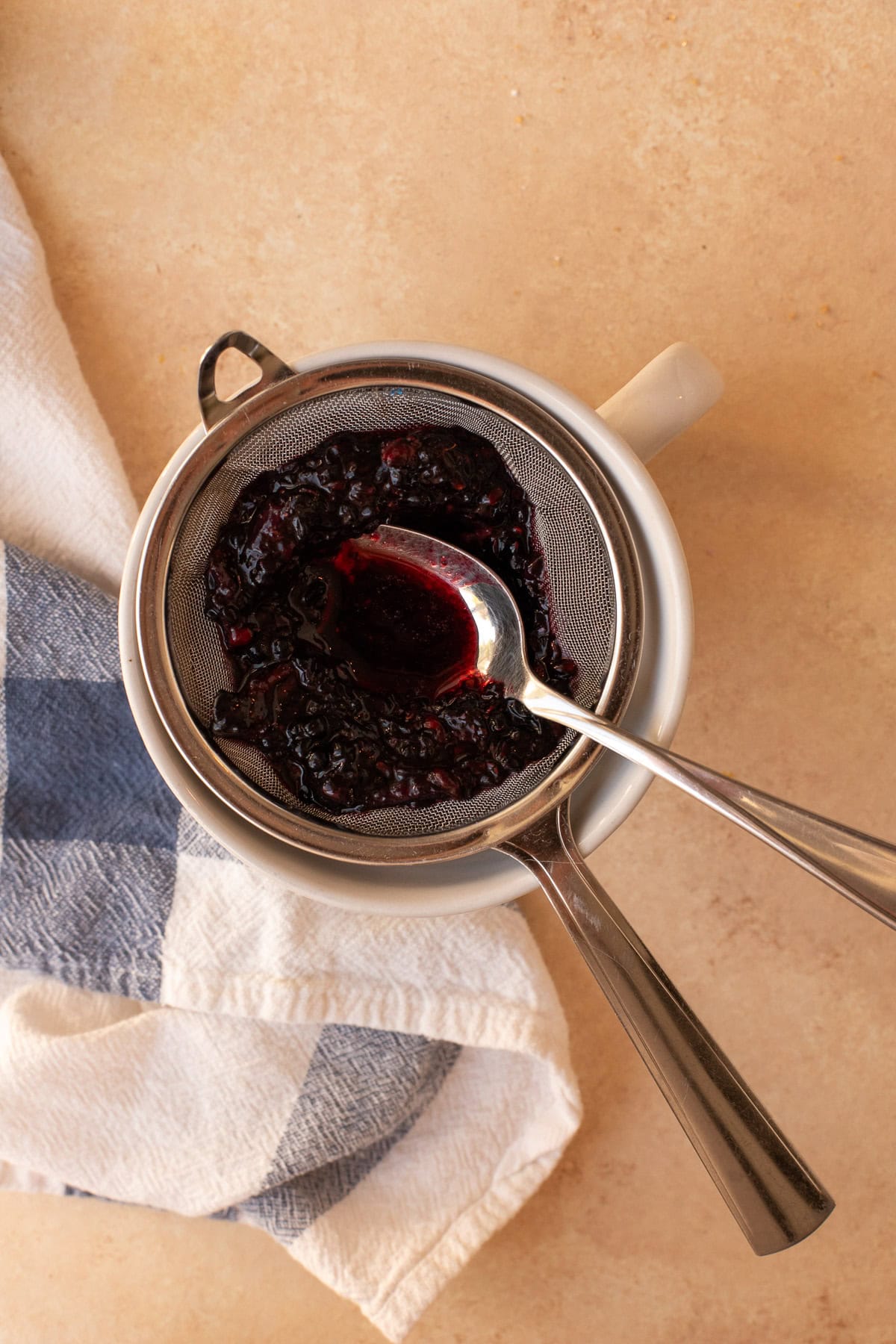 Mashed blackberries being pressed through a small mesh strainer with a spoon.