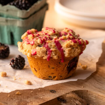 A muffin on a piece of parchment, with individual blackberries scattered nearby.