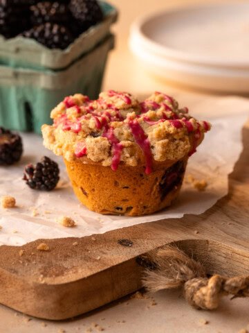 A muffin on a piece of parchment, with individual blackberries scattered nearby.