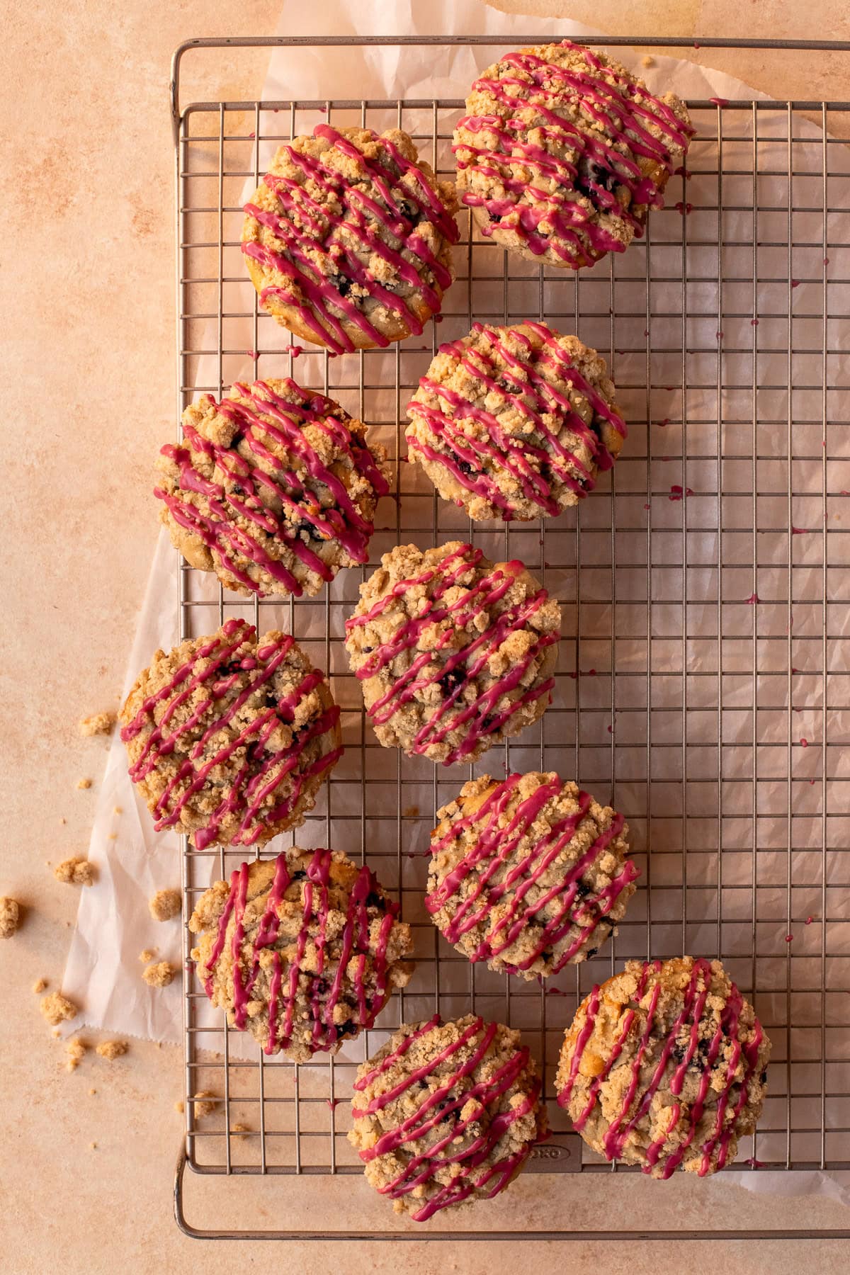 Muffins topped with blackberry icing drizzle over a wire cooling rack.