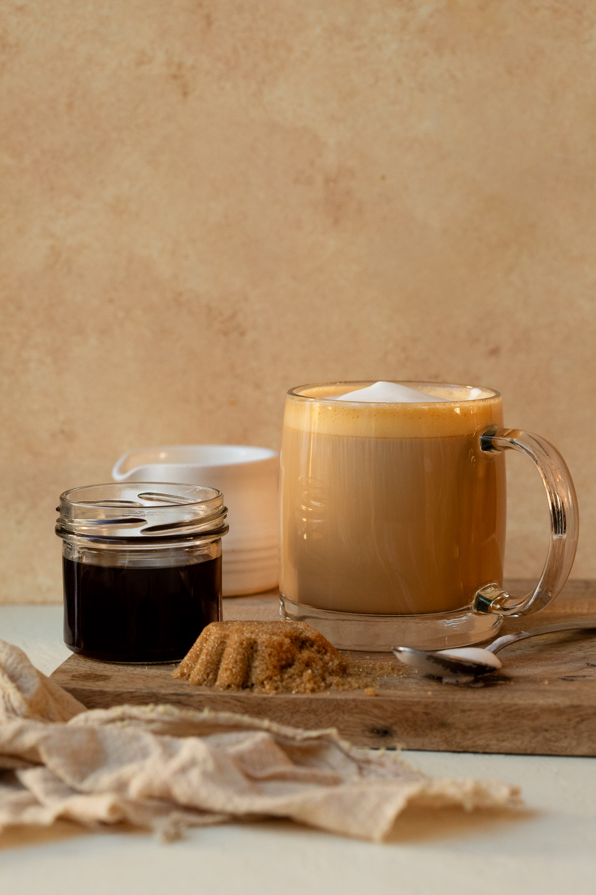 A latte served on a wooden board alongside brown sugar syrup and fresh brown sugar.