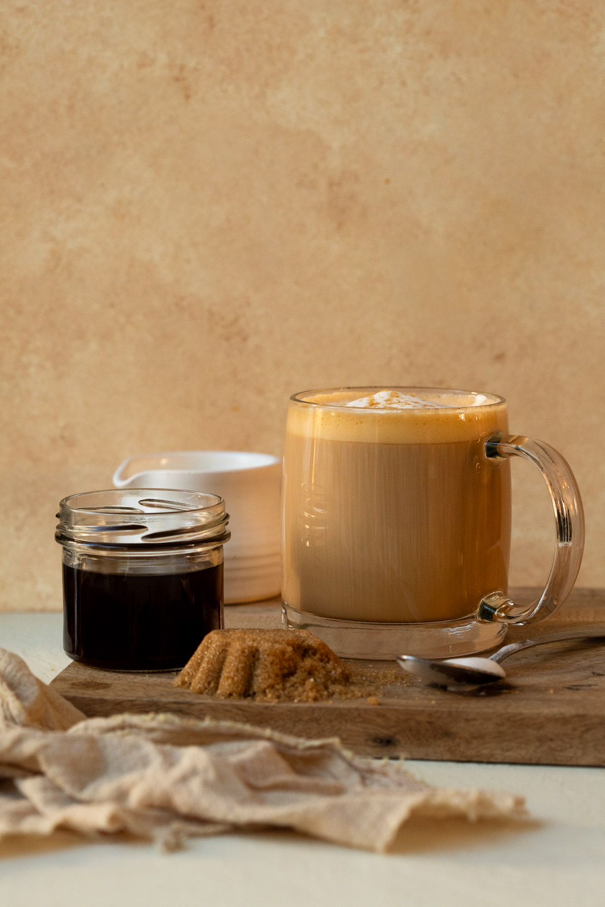 A latte served on a wooden board alongside brown sugar syrup and fresh brown sugar.
