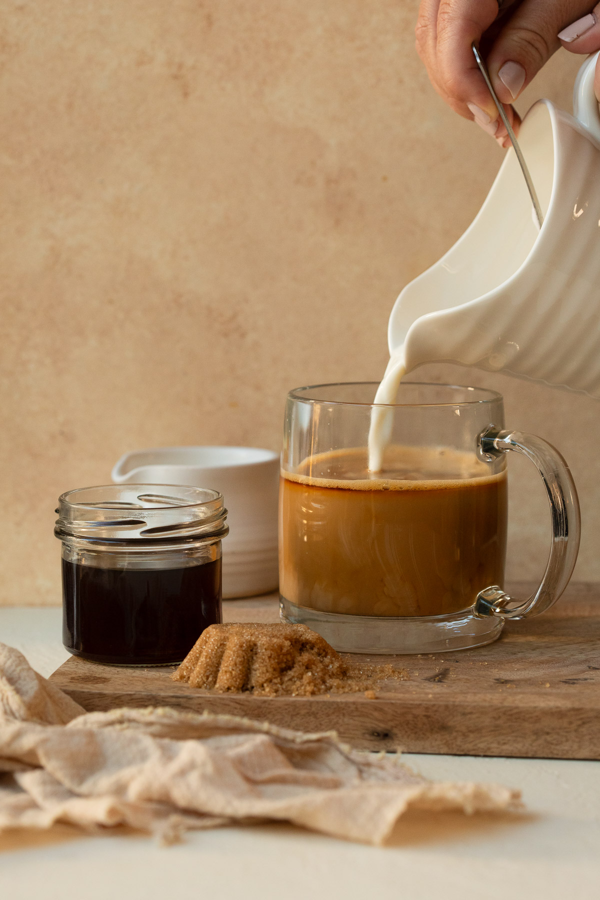 Steamed and frothed milk being poured into espresso in a glass mug.