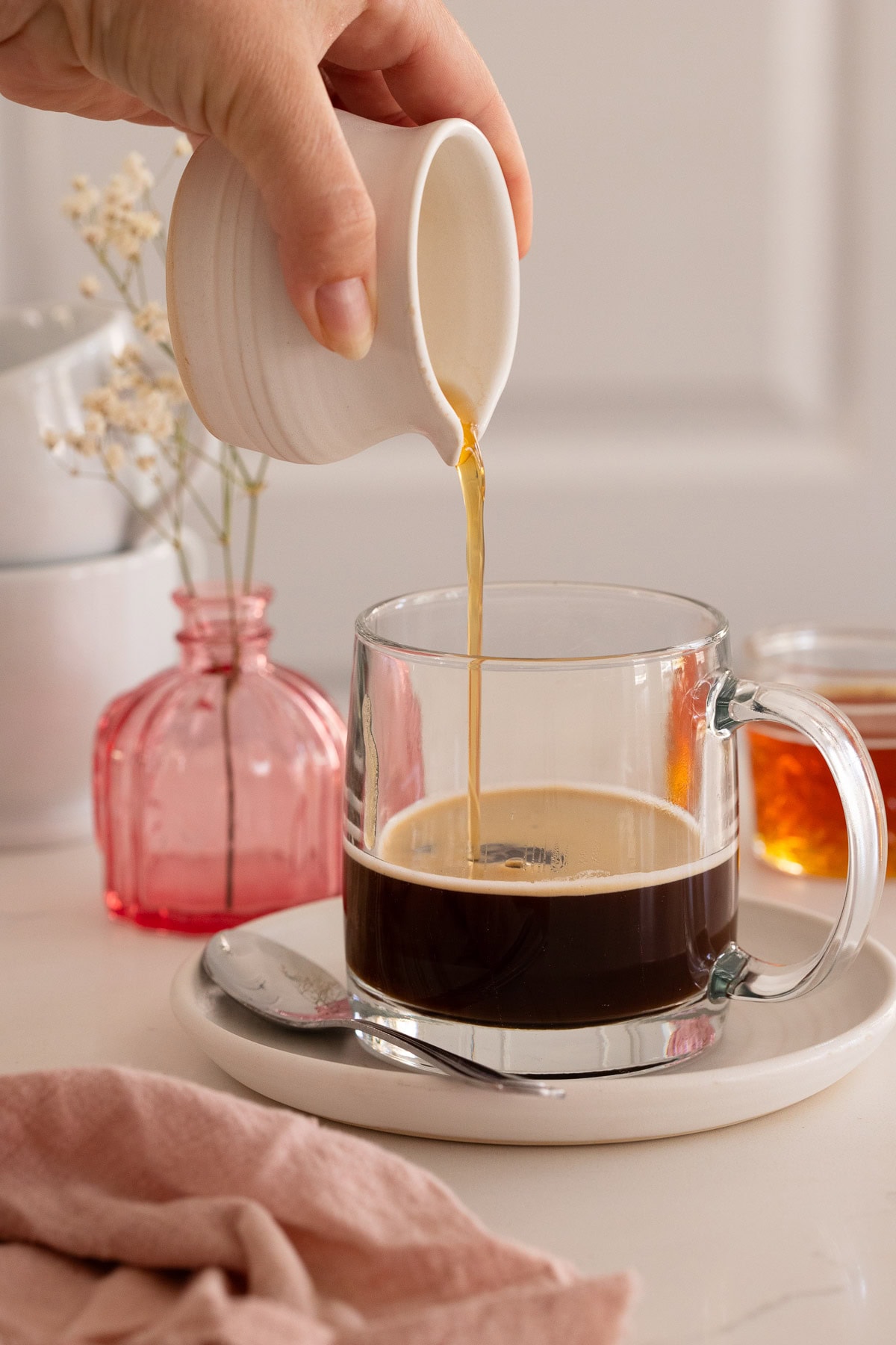 Honey syrup being poured into espresso in a glass mug.