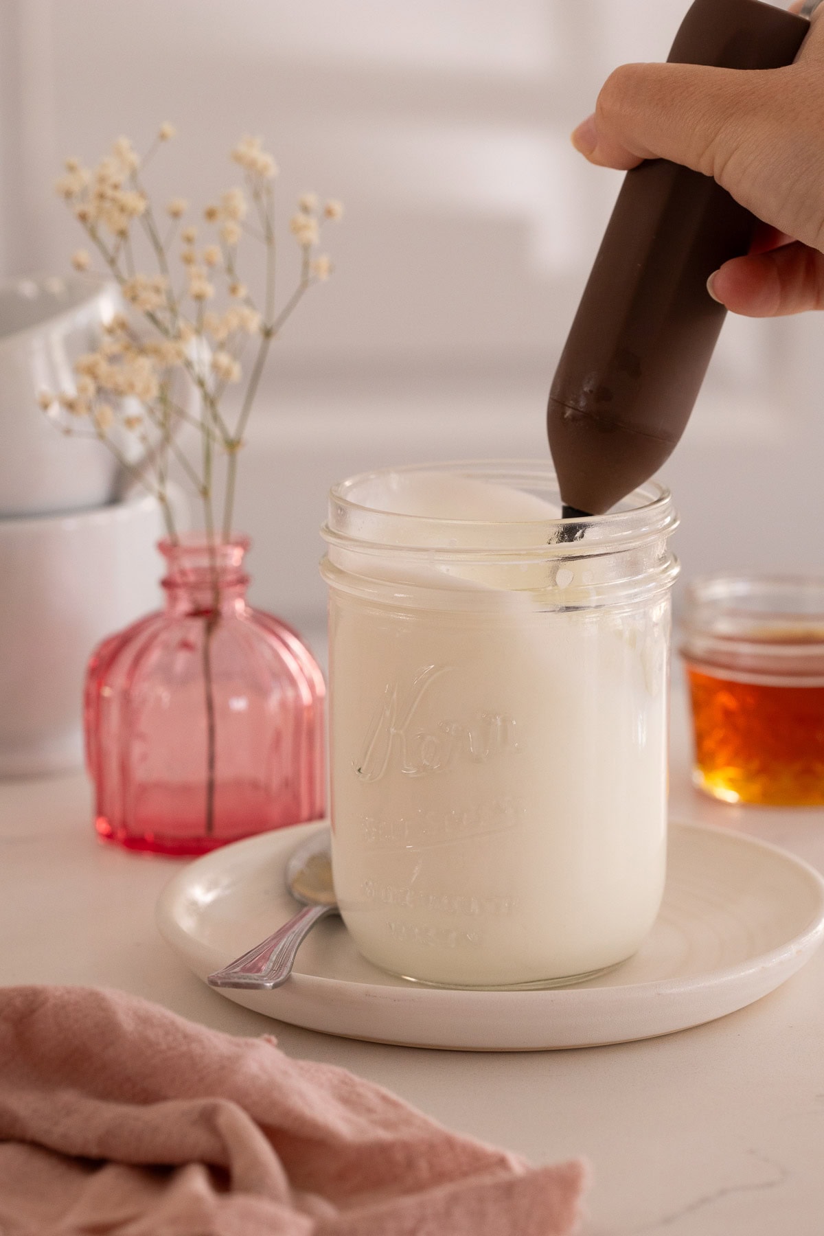 Milk and cream being frothed in a mason jar using a frothing wand.
