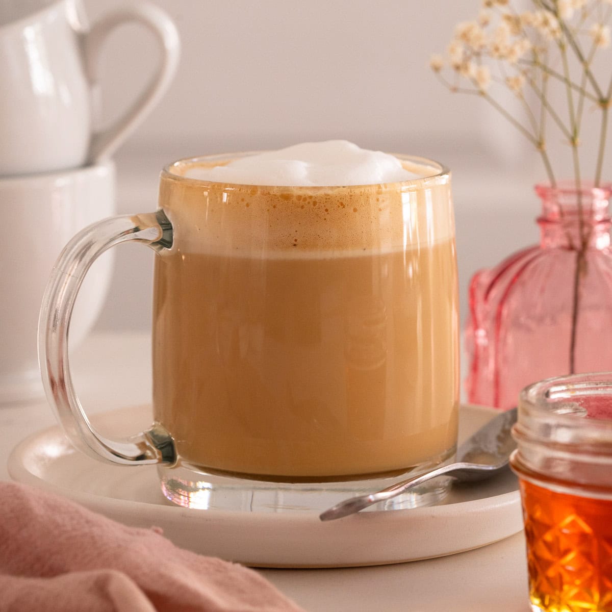 A latte served in a glass mug with a small jar of honey in the foreground.