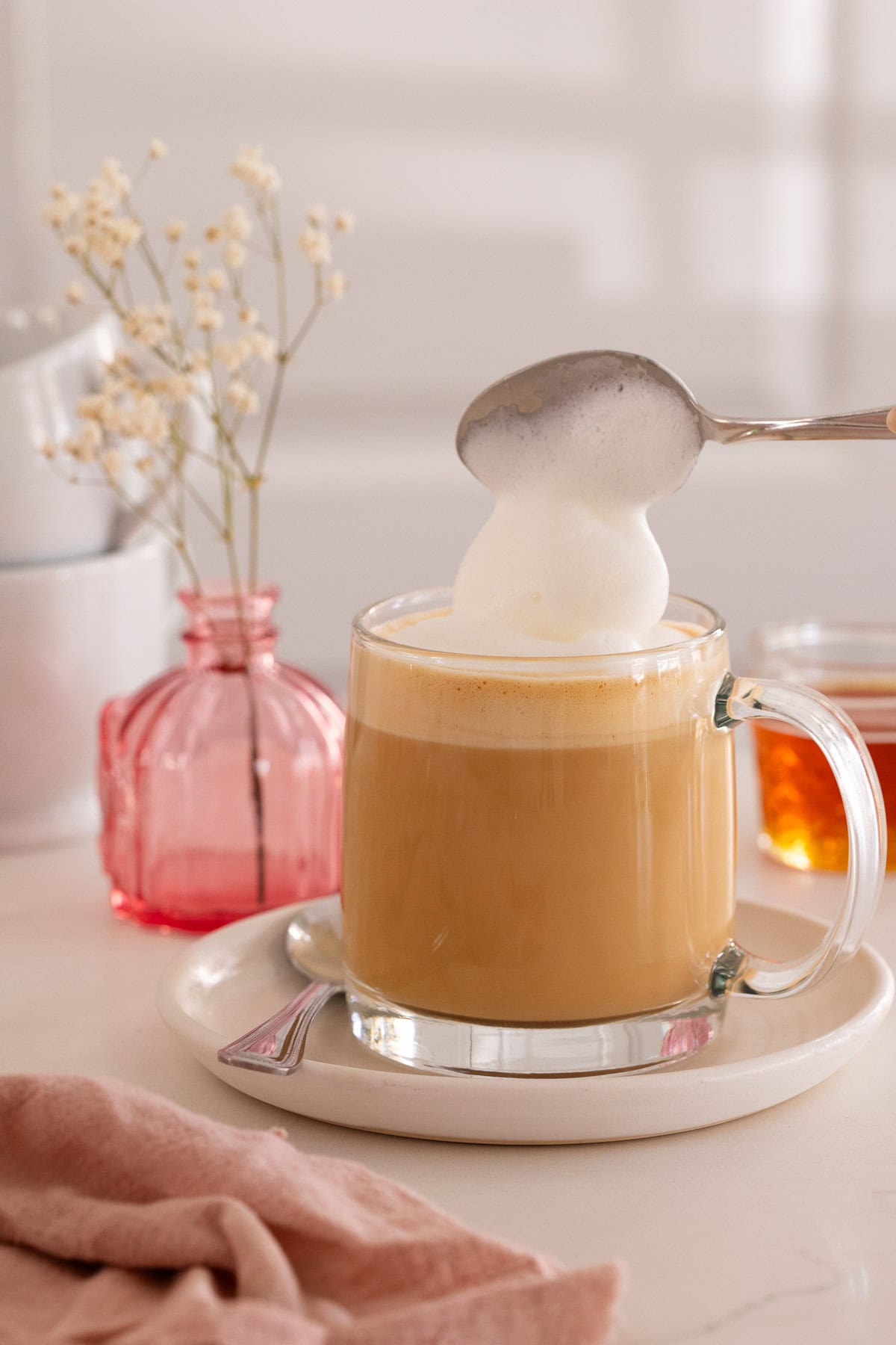 Milk foam being spooned onto a latte in a glass mug.