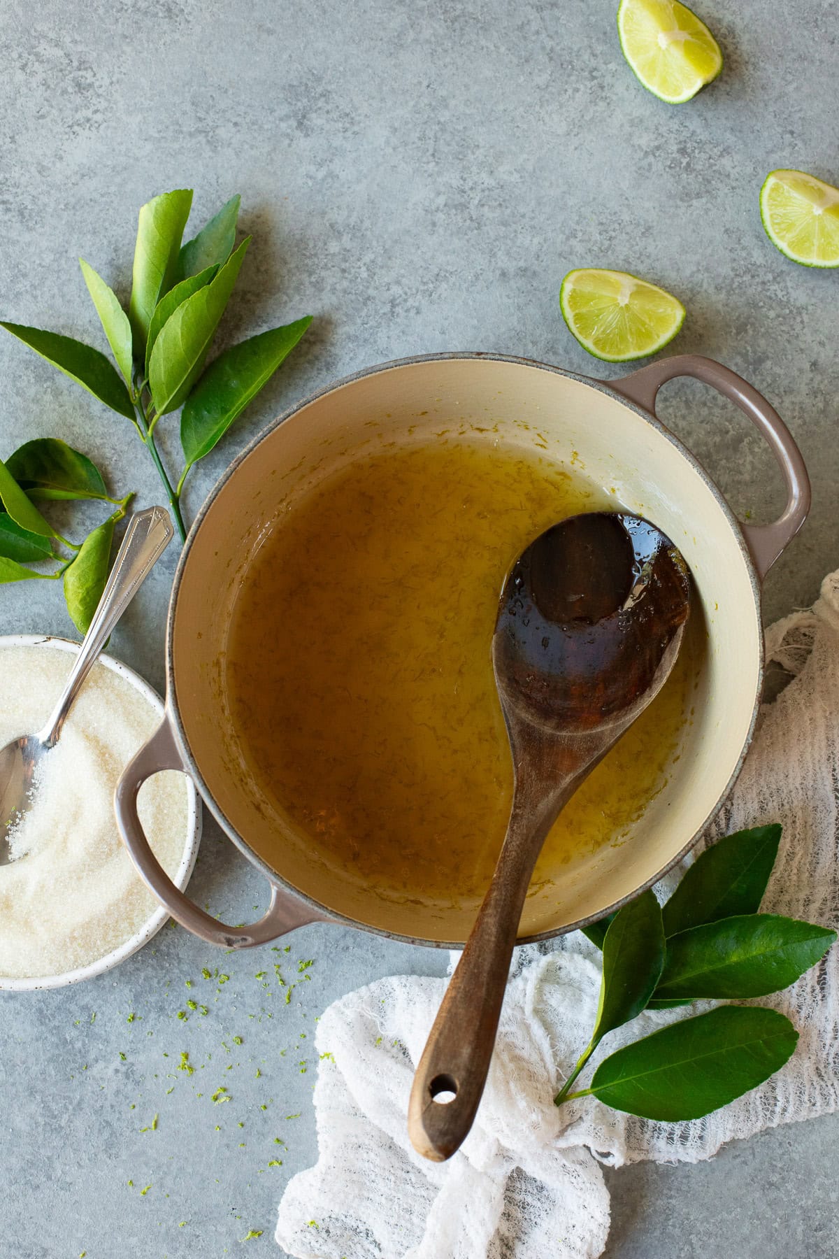 Lime simple syrup after being cooked in a pot, with a wooden spoon in the pan.