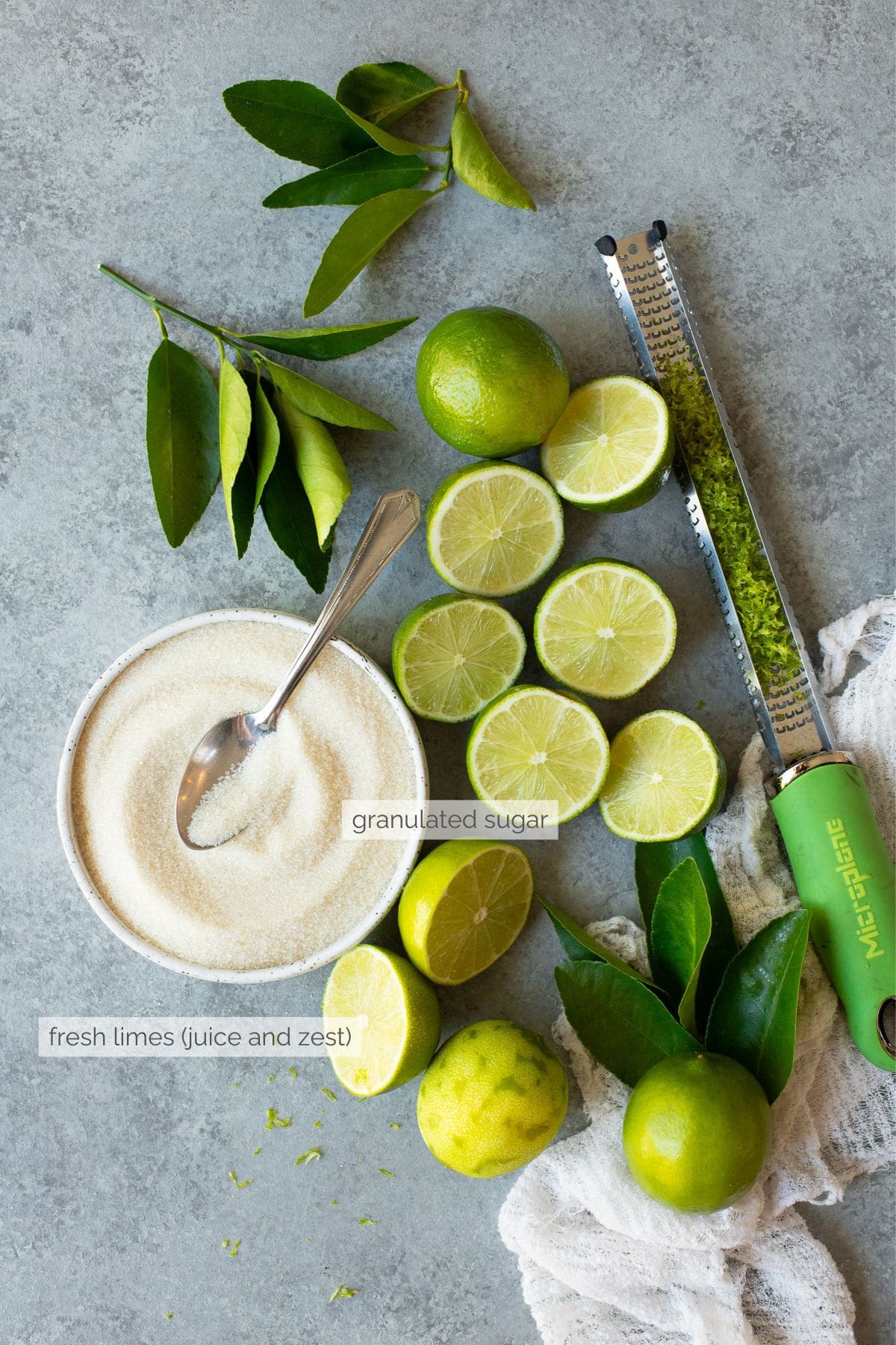 Limes (both whole and sliced, with some zested) and a bowl of granulated sugar.